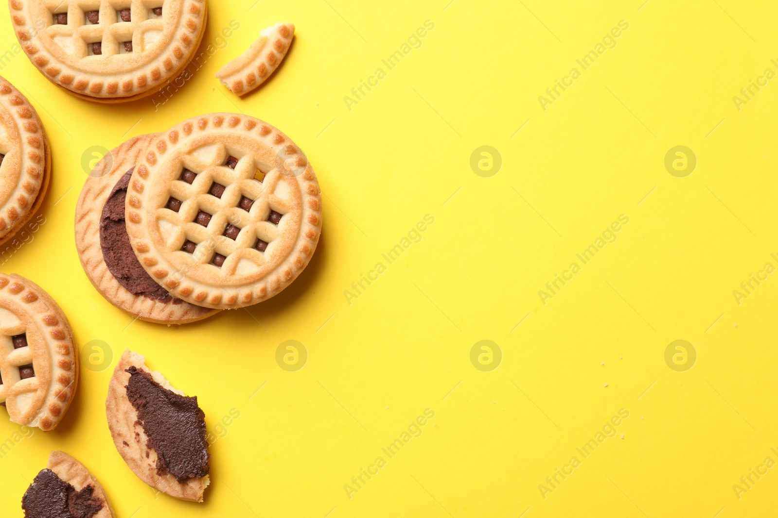 Photo of Tasty sandwich cookies with cream on yellow background, flat lay. Space for text