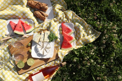 Photo of Picnic blanket with delicious food and wine on green grass outdoors, top view