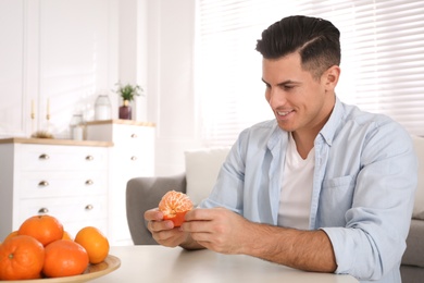 Photo of Happy man peeling tangerine at table indoors