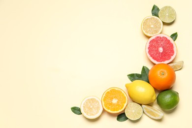 Photo of Different cut citrus fruits and leaves on beige table, flat lay. Space for text