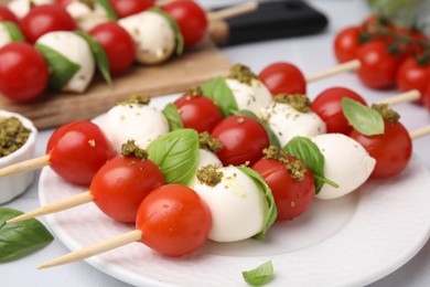 Caprese skewers with tomatoes, mozzarella balls, basil and pesto sauce on table, closeup