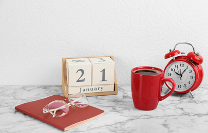 Composition with wooden block calendar and cup of coffee on white marble table