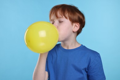 Photo of Boy inflating yellow balloon on light blue background