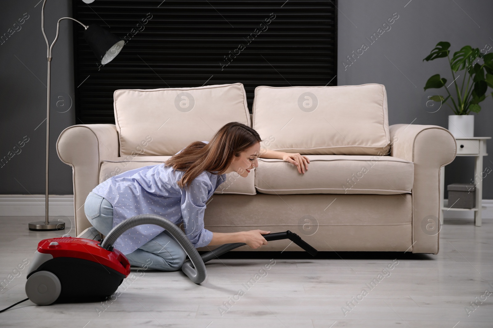 Photo of Young woman using vacuum cleaner at home