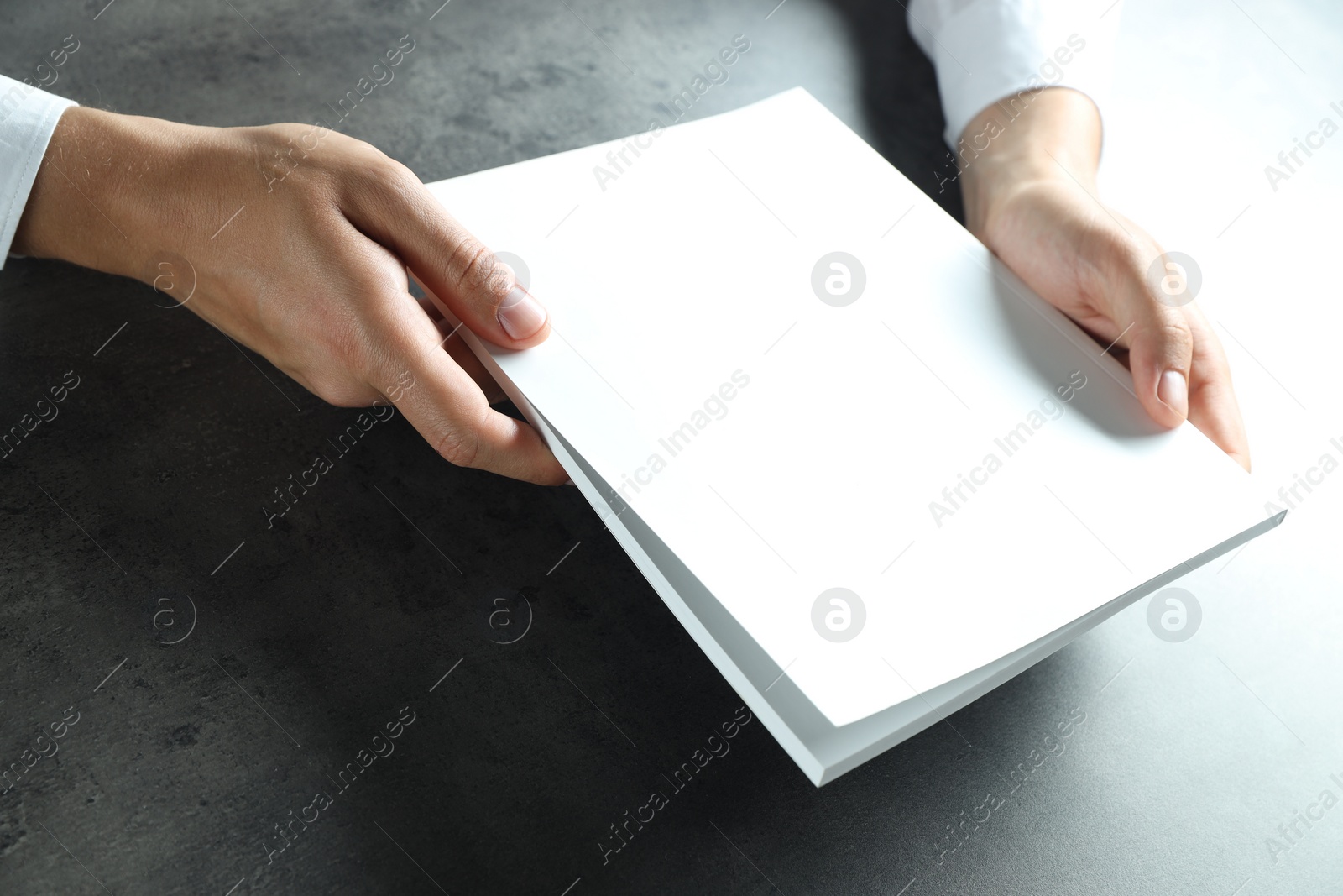 Photo of Man holding blank notebook at black textured table, closeup. Mockup for design