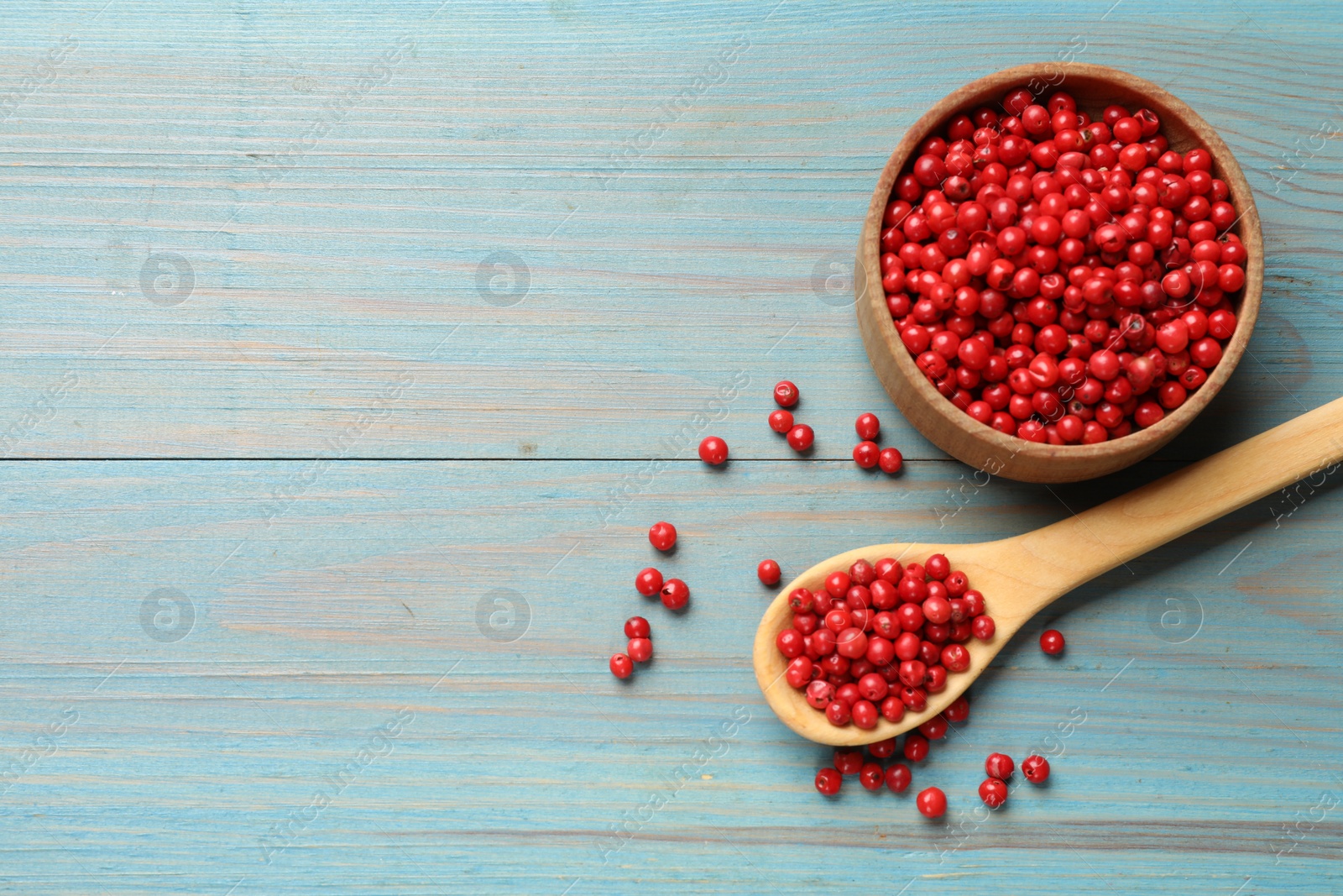 Photo of Aromatic spice. Red pepper in bowl and spoon on light blue wooden table, top view. Space for text