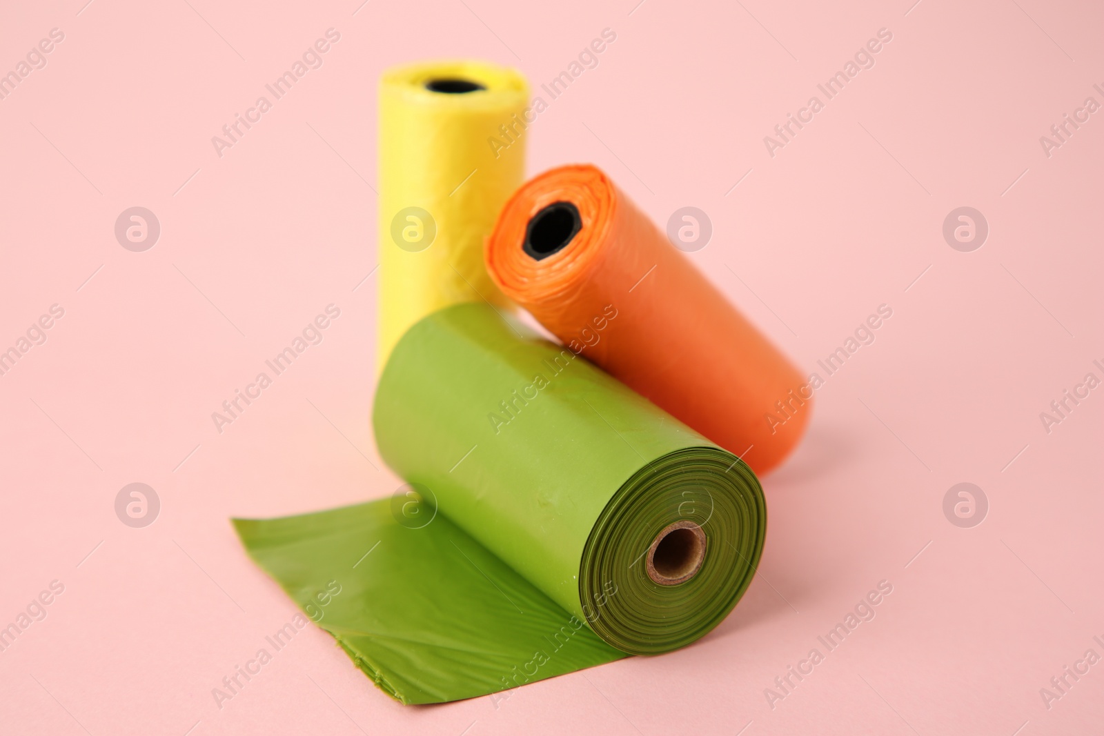 Photo of Colorful dog waste bags on pink background, closeup