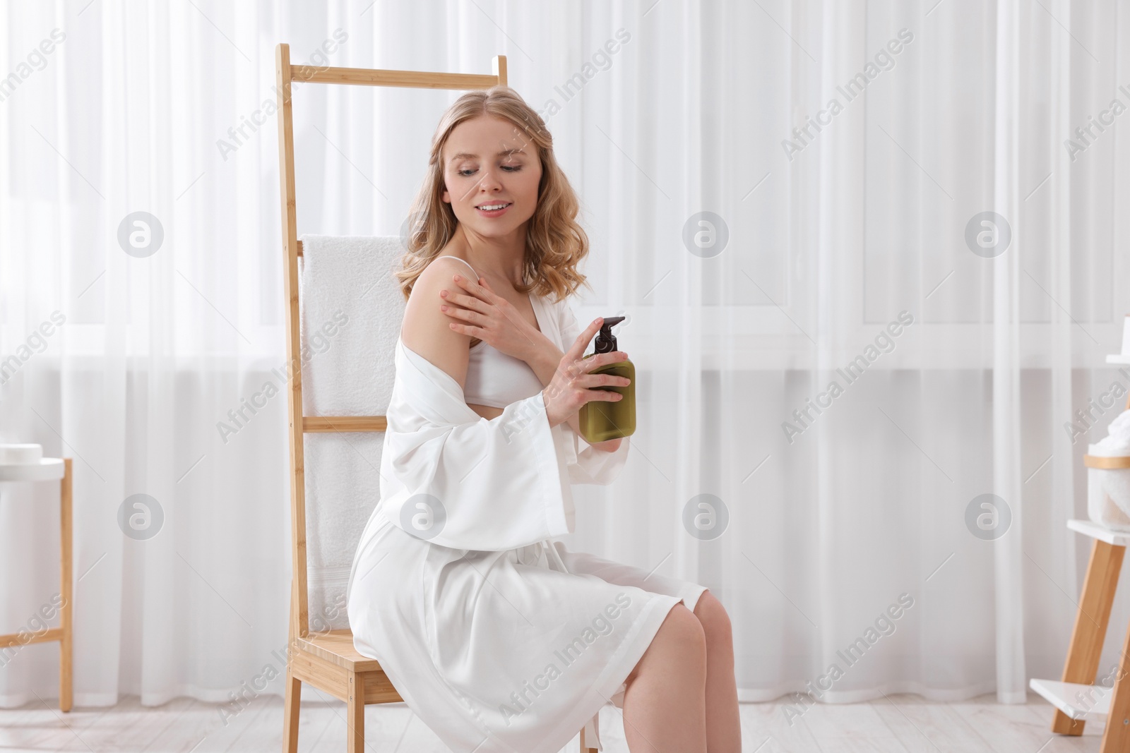 Photo of Beautiful young woman applying oil onto shoulder indoors