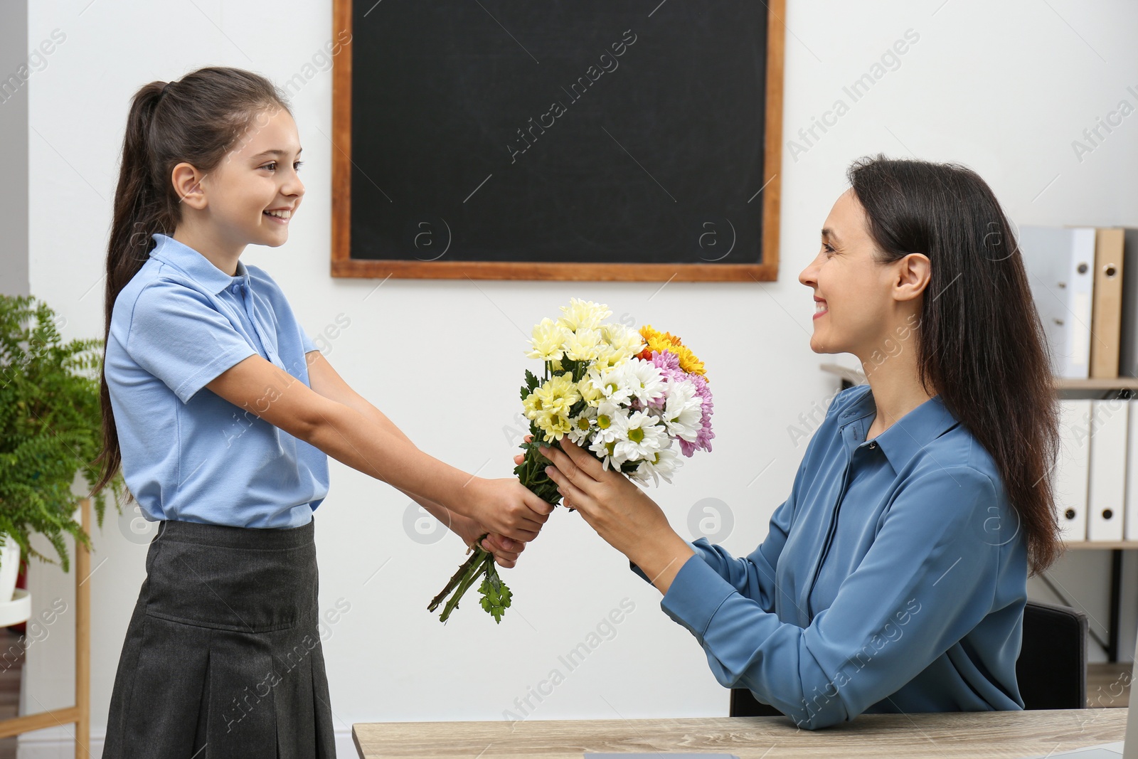 Photo of Schoolgirl congratulating her pedagogue with bouquet in classroom. Teacher's day