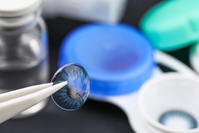 Tweezers with color contact lens over table, closeup. Space for text