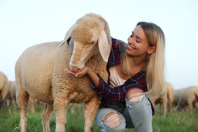 Photo of Smiling woman feeding cute sheep on pasture. Farm animals