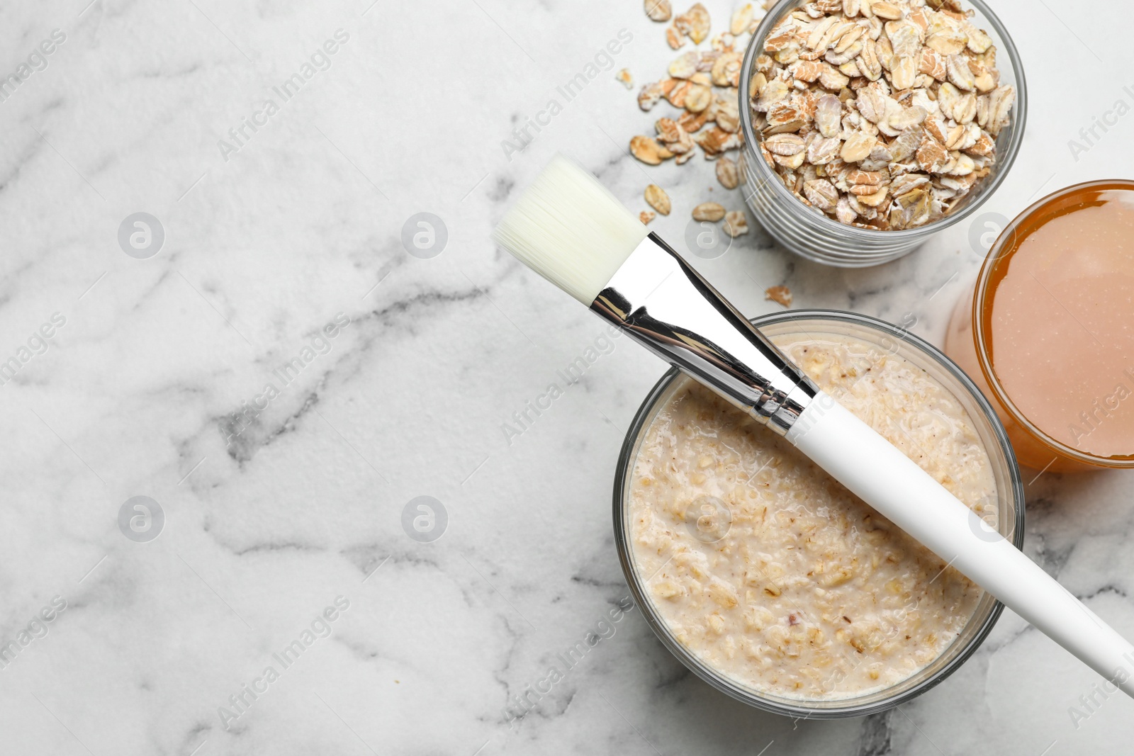 Photo of Handmade face mask made of honey and oatmeal on white marble table, flat lay. Space for text