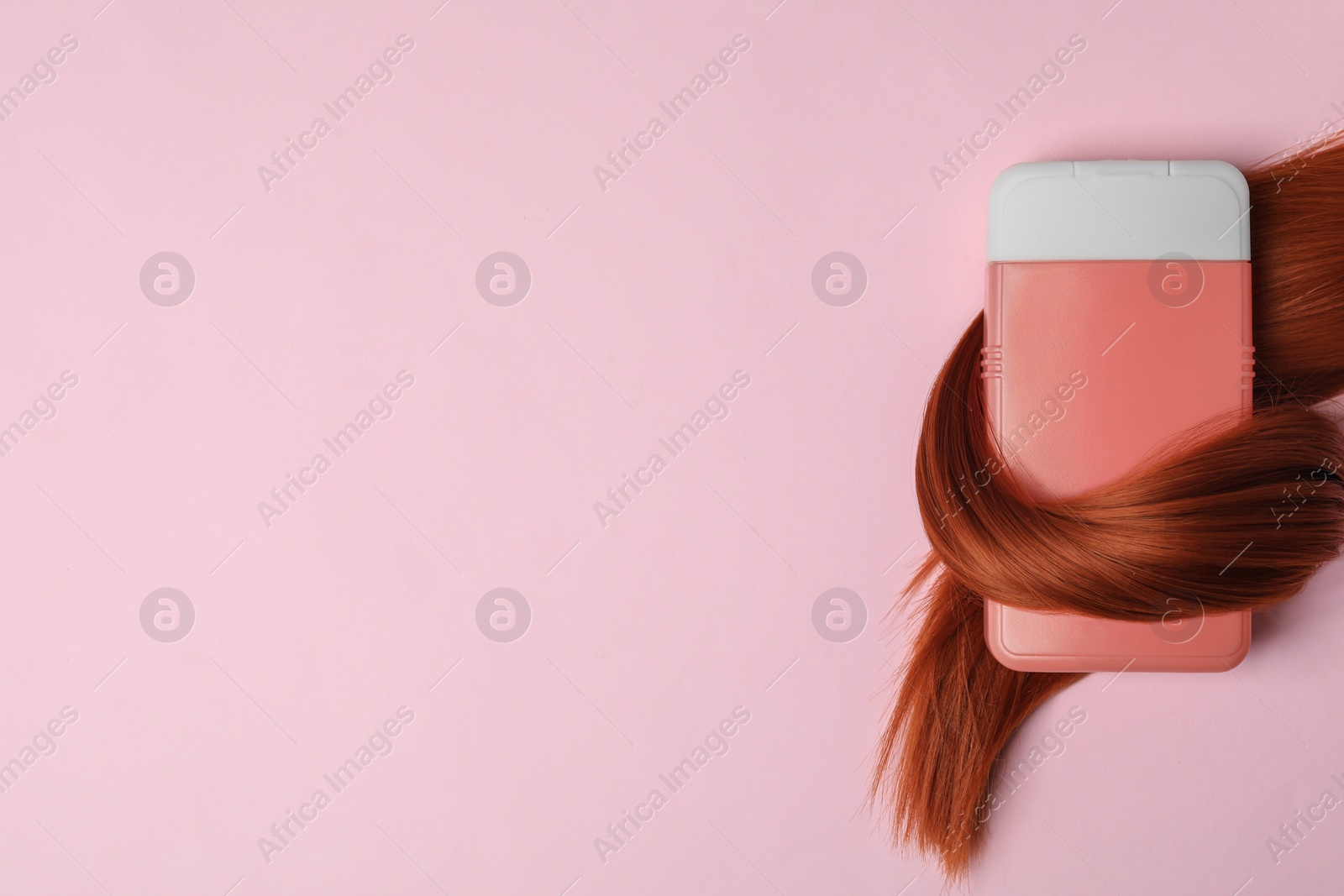 Photo of Shampoo bottle wrapped in lock of hair on pink background, flat lay with space for text. Natural cosmetic products