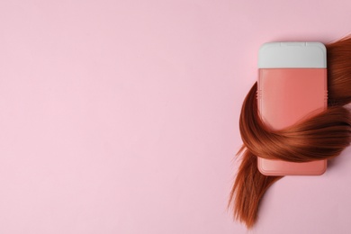 Shampoo bottle wrapped in lock of hair on pink background, flat lay with space for text. Natural cosmetic products