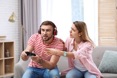 Young man playing video game at home while his girlfriend angry with him