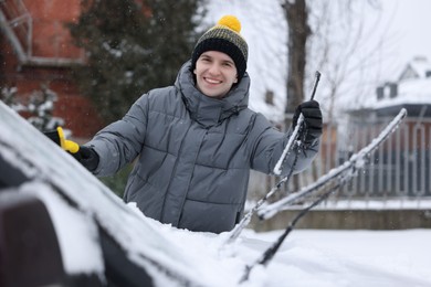 Photo of Man cleaning snow from car with brush outdoors