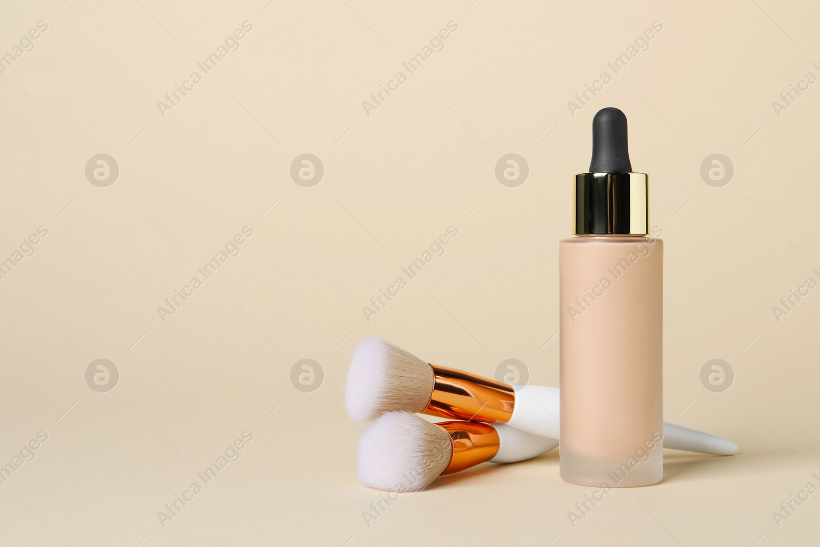Photo of Bottle of skin foundation and brushes on beige background, space for text. Makeup product