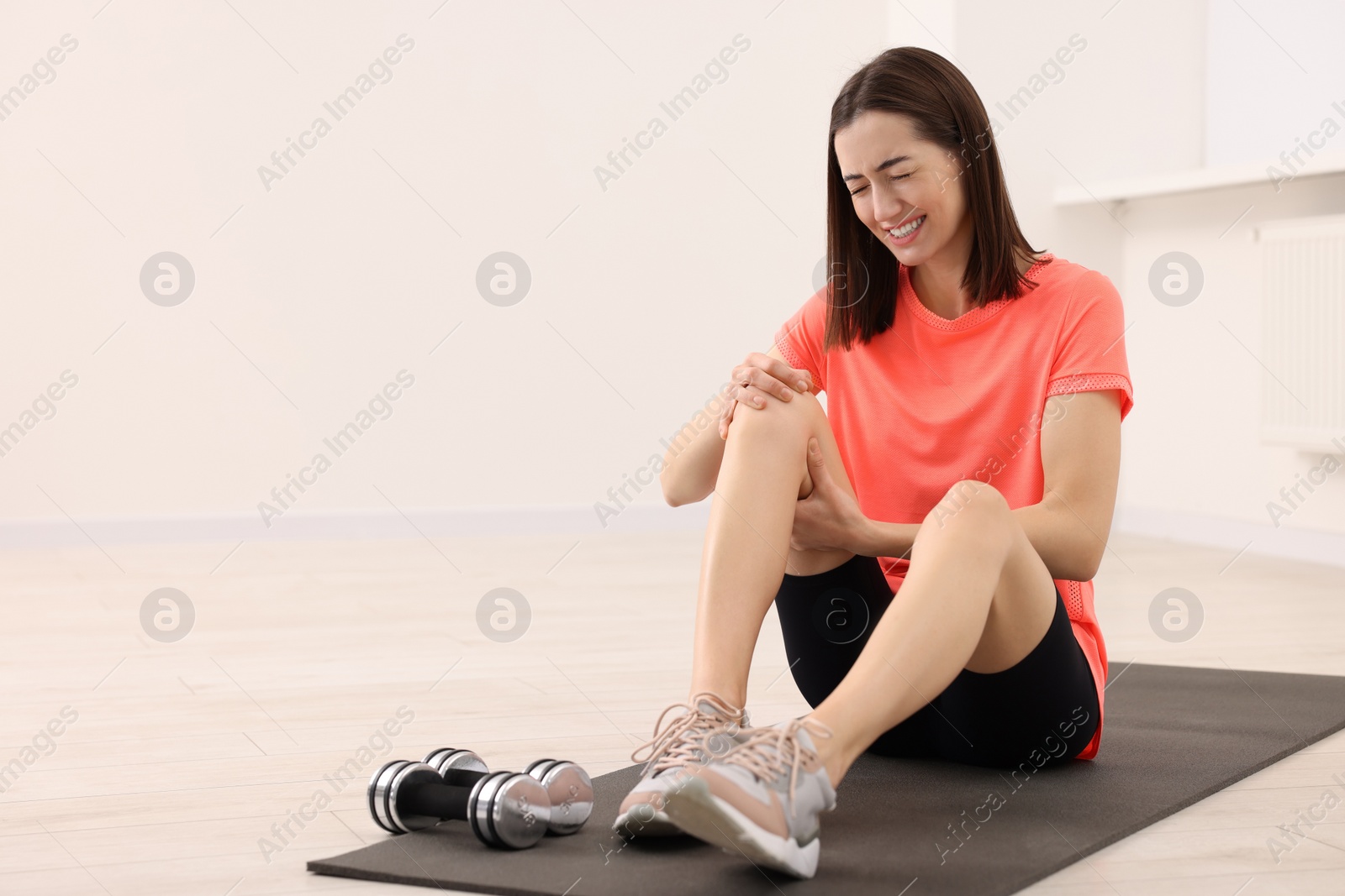 Photo of Young woman suffering from leg pain on exercise mat indoors, space for text