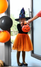 Photo of Cute little girl dressed as witch trick-or-treating at doorway. Halloween tradition