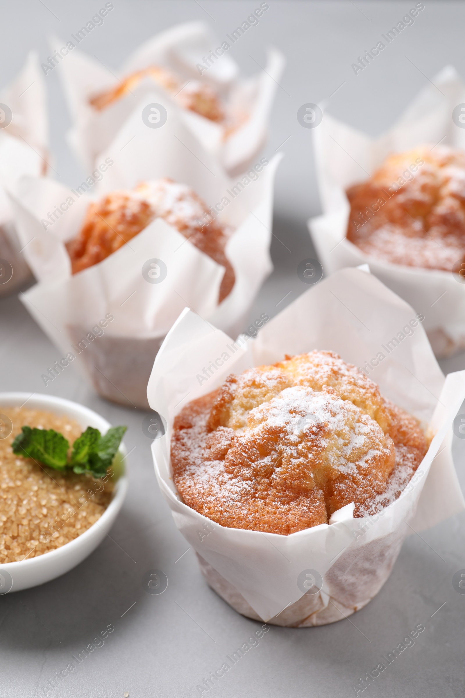 Photo of Delicious muffins with powdered sugar on grey table, closeup