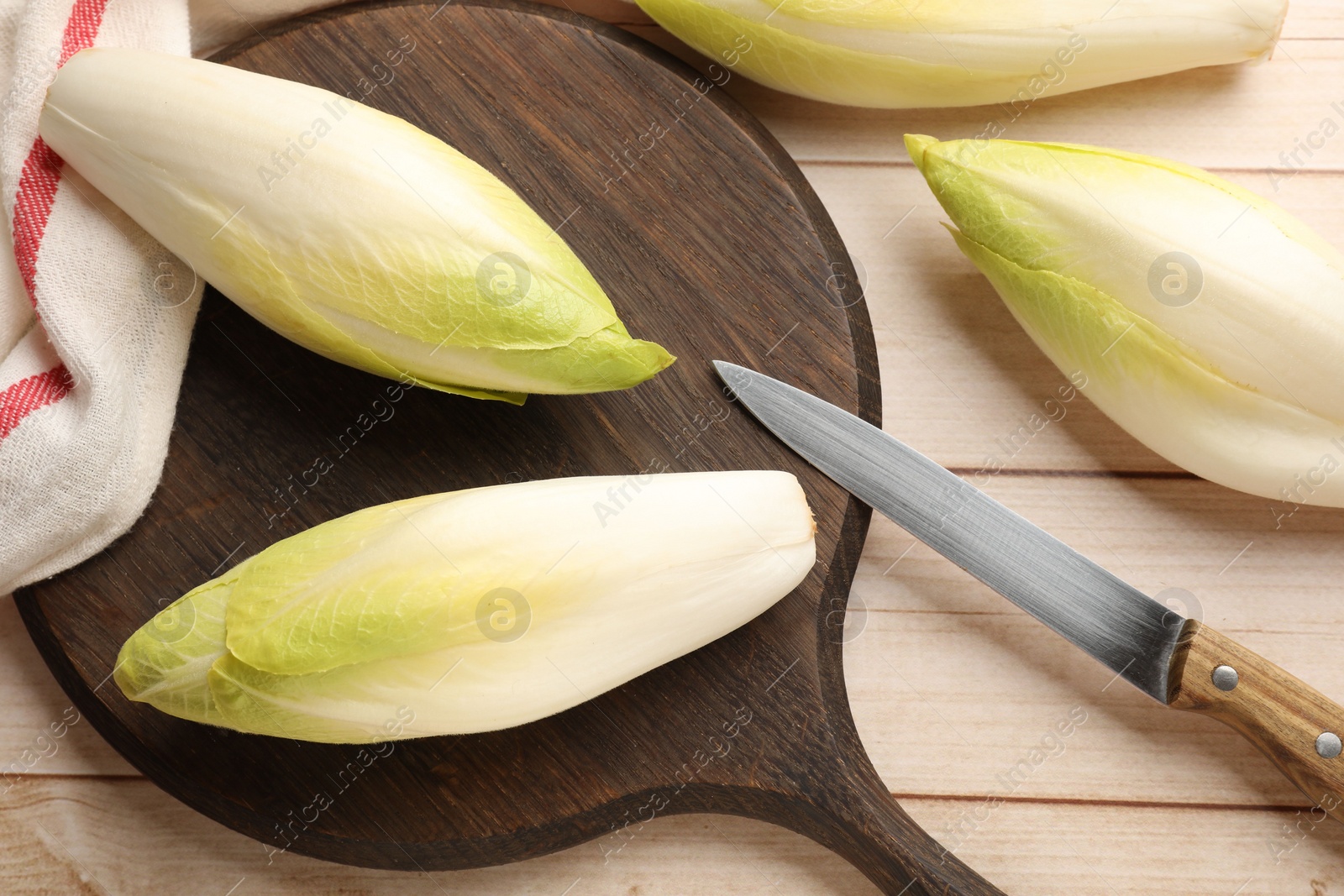 Photo of Raw ripe chicories and knife on wooden table, top view