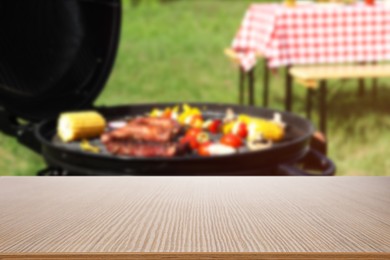 Image of Empty wooden table and blurred view of tasty food on modern barbecue grill outdoors
