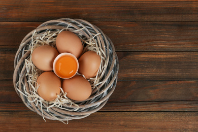 Photo of Raw chicken eggs in wicker nest on wooden table, top view