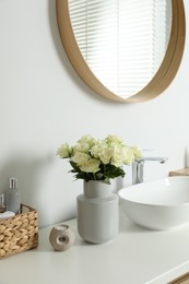 Photo of Vase with beautiful white roses and toiletries near sink in bathroom