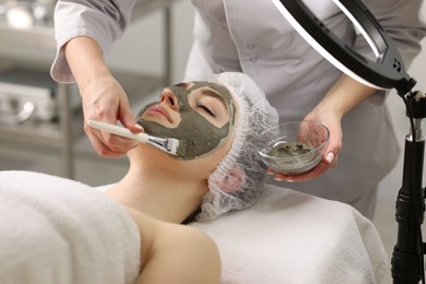 Photo of Cosmetologist applying mask on woman's face in clinic, closeup