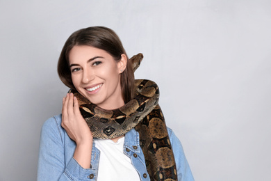 Photo of Young woman with boa constrictor on light background, space for text. Exotic pet