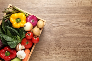 Photo of Fresh vegetables in crate on wooden table, top view. Space for text