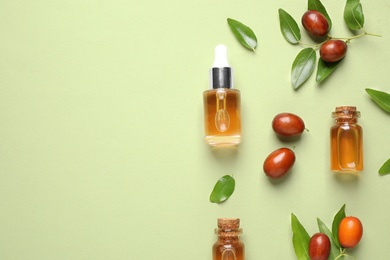 Glass bottles with jojoba oil and seeds on green background, flat lay. Space for text