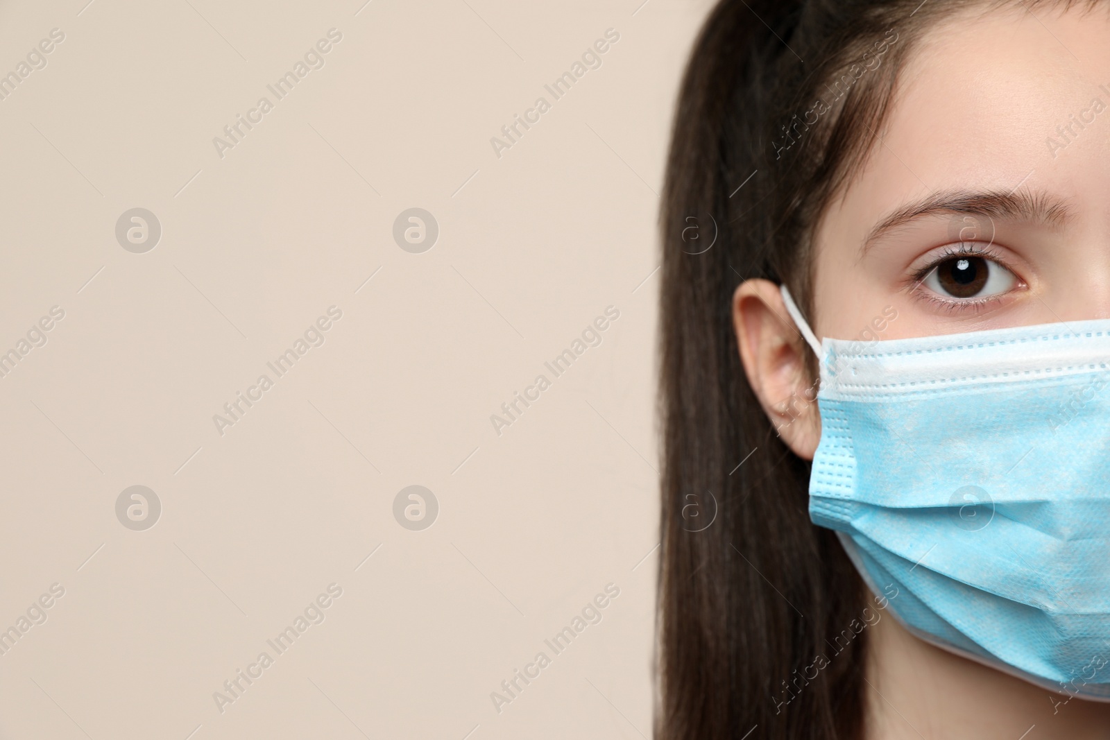 Photo of Little girl in medical mask on beige background, closeup with space for text. Virus protection