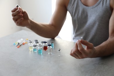 Photo of Man with syringe and many different vials at table indoors, closeup. Doping concept