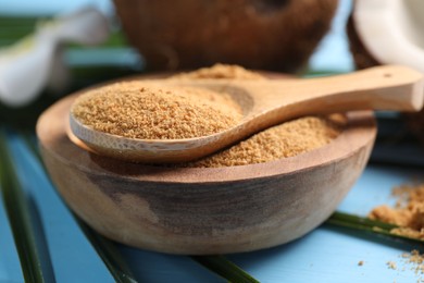 Photo of Coconut sugar in bowl, spoon and fruits on light blue wooden table, closeup