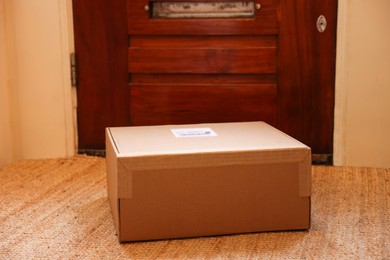 Photo of Delivery service. Cardboard on rug near wooden door indoors