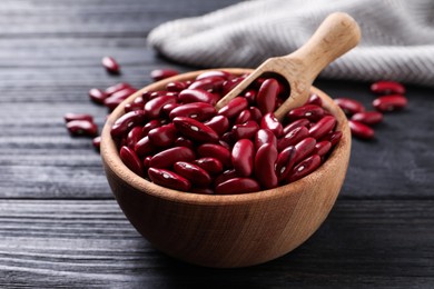 Photo of Raw red kidney beans in bowl and scoop on dark wooden table, closeup