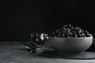 Photo of Bowl of delicious ripe black mulberries on grey table, space for text