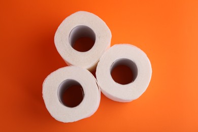 Photo of Soft toilet paper rolls on orange background, flat lay