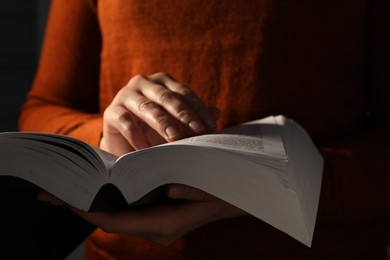 Woman reading Bible against black background, closeup
