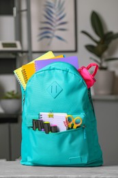 Photo of Turquoise backpack with different school stationery on table indoors