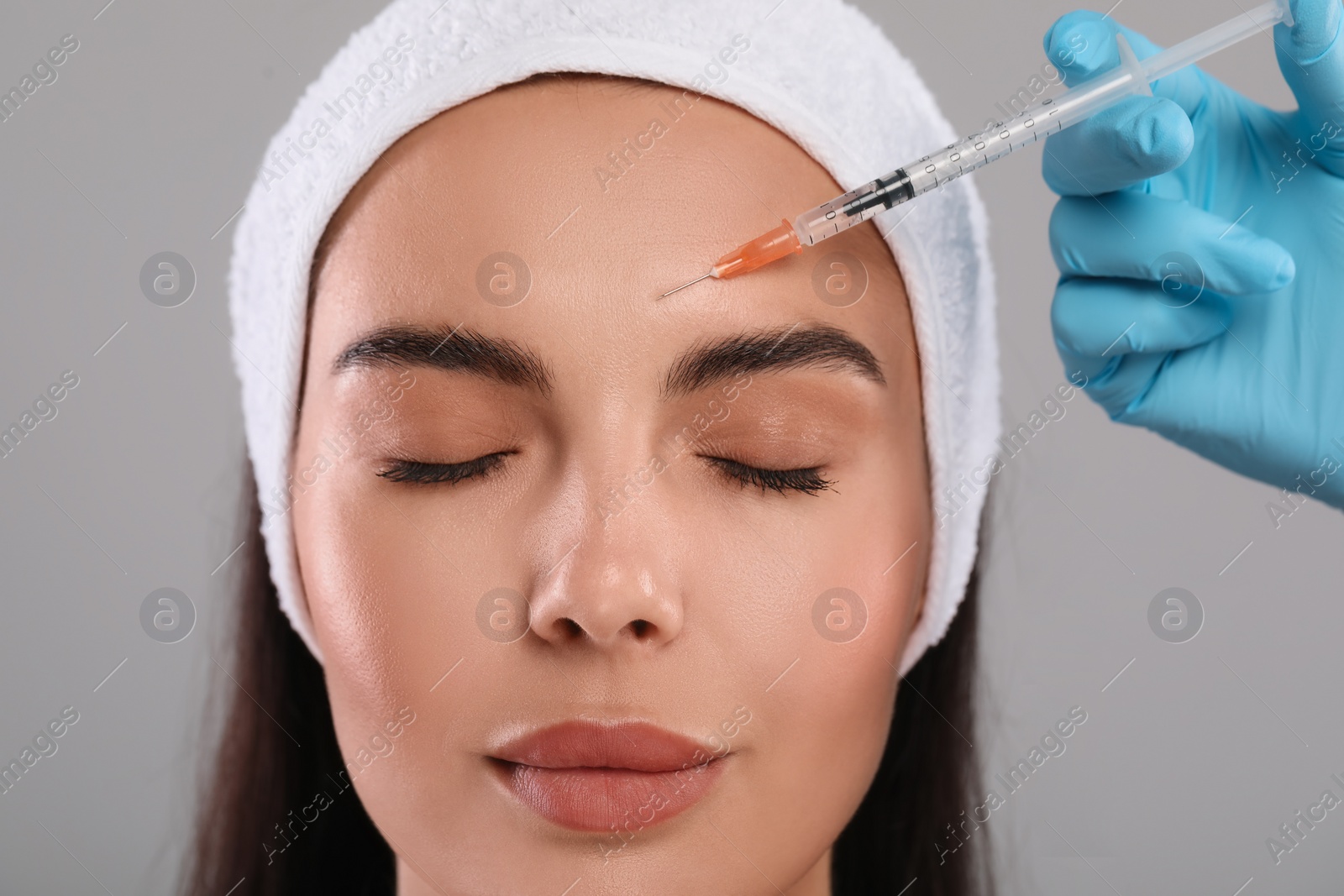 Photo of Doctor giving facial injection to young woman on light grey background, closeup. Cosmetic surgery