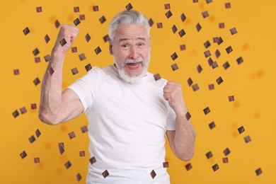 Happy man under flying confetti on orange background