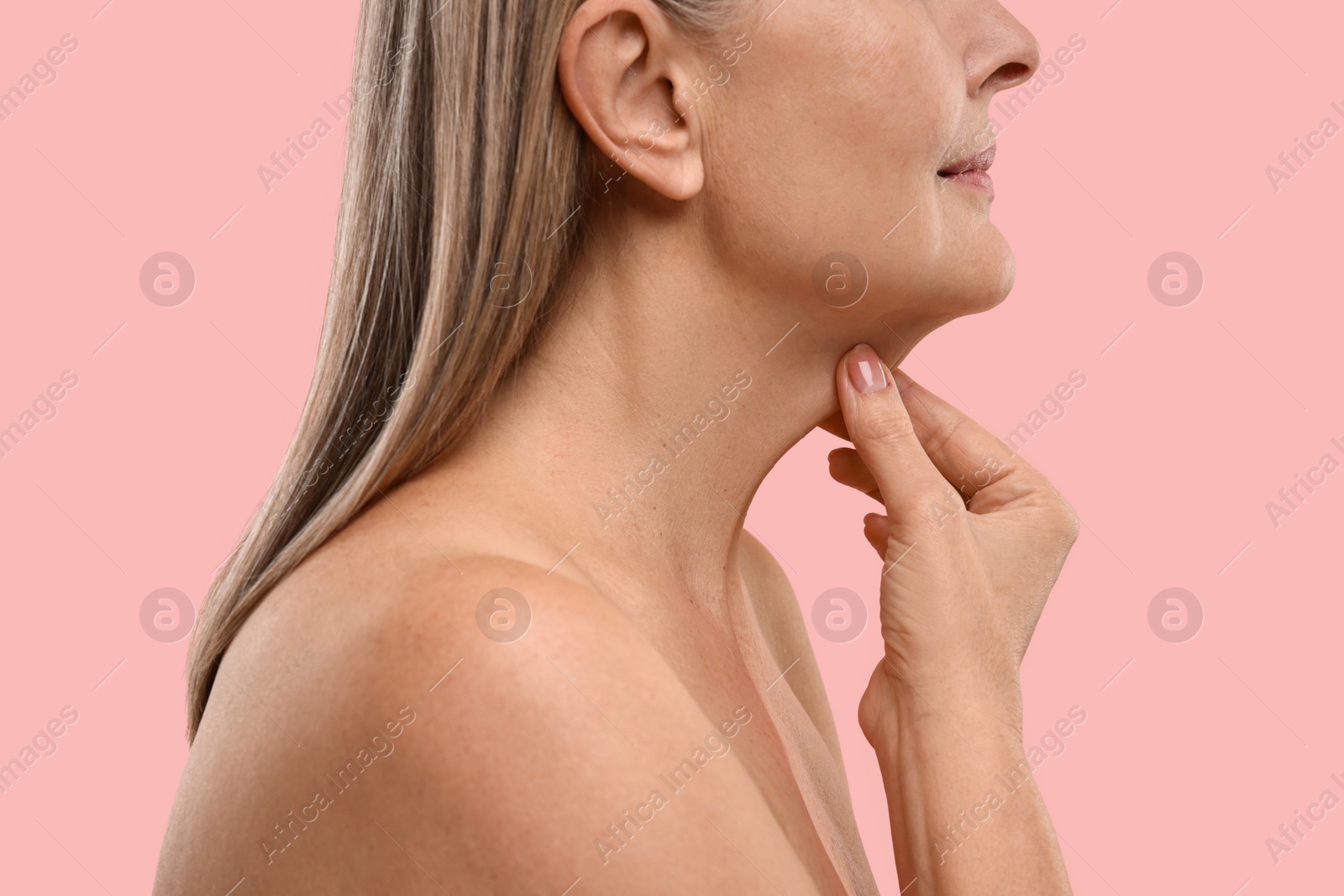 Photo of Mature woman touching her neck on pink background, closeup