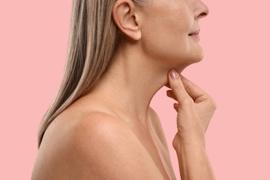 Mature woman touching her neck on pink background, closeup