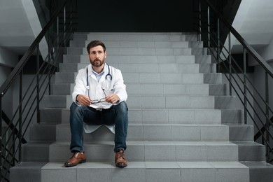 Photo of Doctor sitting on stairs in hospital. Space for text