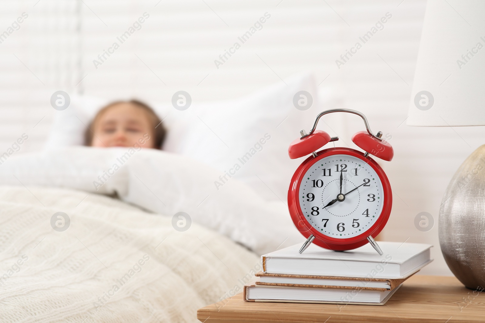 Photo of Cute little girl awaking in cosy bed, focus on alarm clock