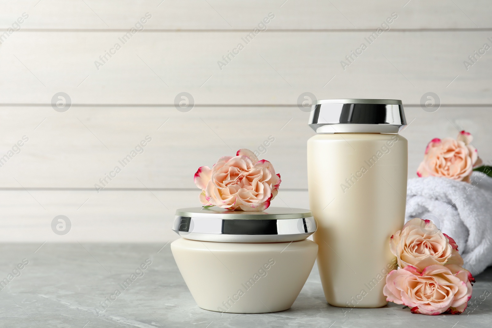 Photo of Hair care cosmetic products and flowers on light grey marble table, space for text
