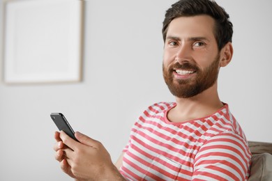 Photo of Handsome bearded man using smartphone at home