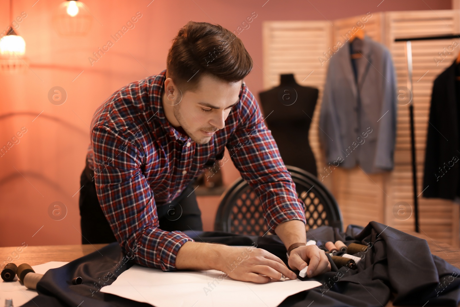 Photo of Young tailor working with sewing pattern in atelier